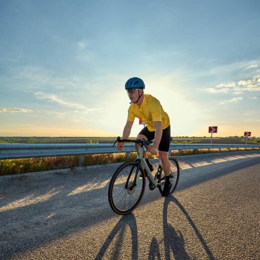 Bisikletçi açık yolda tek başına giderken ufuk görüş açısıyla dengesini ve hareketini gösteriyor. Spor kavramı, özgürlük, bireysel mücadele, fitness motivasyonu, açık hava aktivitesi.