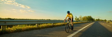 Bisikletli pedalları soluk ışığın altına itiyor, asfalt desenler ve çizgiler mesafeye çıkıyor. Hareket bulanıklığı etkisi. Pankart. Profesyonel spor, egzersiz, denge, odaklanma, yol enerjisi kavramı.