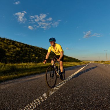Altın güneş ışığı asfalt ve yeşil tepeler çizgisi yolundan yansır gibi sakin bir ifadeyle, bisikletçi sürekli olarak açık otoyolda ilerler. Spor anlayışı, bisiklet, sağlıklı yaşam tarzı, doğa.