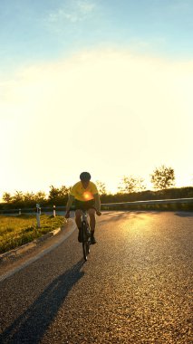 Arka aydınlatma motorcuları, yoğun akşam antrenmanının bir parçası olarak, parlak güneşli yolda yol kıvrımlarını takip ediyorlar. Spor, bisiklet, rekabet, eğitim, güç, dayanıklılık kavramı.