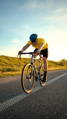 Adam yokuş yukarı sürat sürüşü sırasında gidona ve pedallara yaslanıyor, temiz gökyüzüne ve yumuşak araziye karşı çaba gösteriyor ve odaklanıyor. Spor, bisiklet, rekabet, eğitim, hız, güç kavramı.