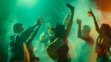 Bir grup insan renkli bir kulüp ortamında duman ve ışıklarla dans edip içki yetiştiriyor. Gece hayatı kavramı, parti, gençlik, yaz, şenlik, kutlama