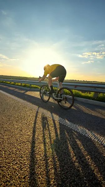 Düşük açılı çekimde bisikletçi sıcak güneşin altında uzun bir gölge yaratıyor ve hareket halindeki güçle pedal çeviriyor. Enerji, hareket, spor atmosferi, motivasyon, çaba ve gündoğumu eğitim yolculuğu kavramı.