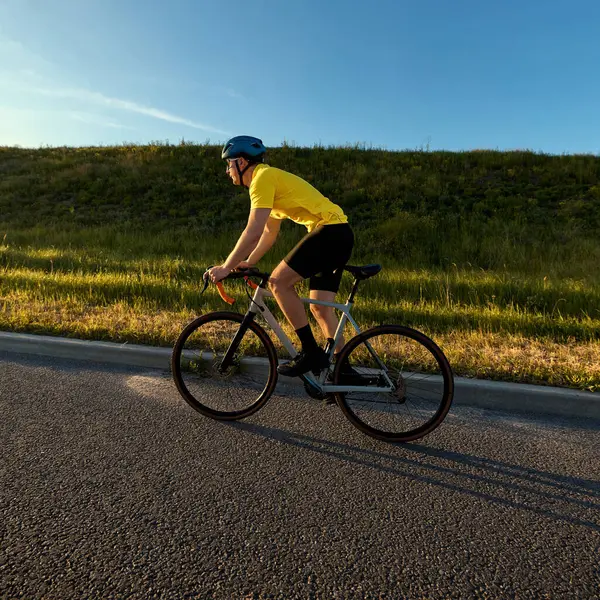 Parlak vitesli bisikletli süvari, temiz mavi gökyüzü altında çimenli arazinin yakınında altın bir akşam ışığı ve nazik bir hareket duyusuyla dönüyor. Spor anlayışı, bisiklet, sağlıklı yaşam tarzı, dayanıklılık, doğa.