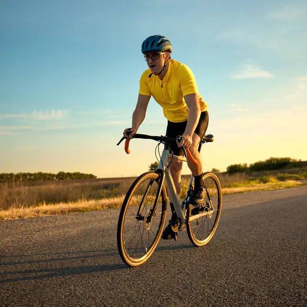 Sarı formalı sporcu, gün batımında düz arazide güçlü bir şekilde nefes alarak yarış antrenmanı yaparken öne doğru itiyor. Spor, bisiklet, rekabet, yarış, eğitim, yoğunluk kavramı