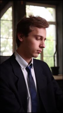 Sivri siyah takım elbiseli kendine güvenen genç adam internette çalışıyor. Laptopuna şık ve modern bir ofiste odaklanmış. Çağdaş mesleki başarı, liderlik, finans kavramı.