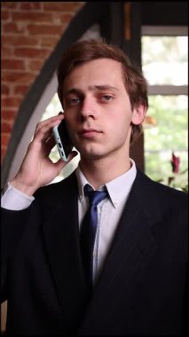 Resmi siyah takım elbiseli genç yönetici telefonu kulağına tutuyor. Gözler yoğunlukta daralıyor. Modern çalışma ortamında profesyonel çağrıyla yakından ilgileniyor. İş anlayışı, iletişim