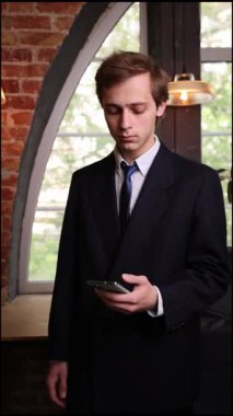 Resmi takım elbiseli kendine güvenen işadamı modern ofiste sakince oturur, akıllı telefondan odaklanarak kayar, mesajları kontrol eder ya da iş güncellemelerini gözden geçirir. İş kavramı, başarı.