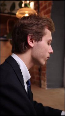 Kendine güvenen, parlak siyah takım elbiseli genç profesyonel, modern ofis alanında oturan, yoğun ifadeli bir dizüstü bilgisayarla çalışıyor. İş kavramı, yatırımlar, uzaktan çalışma.