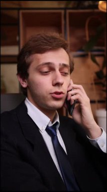 Zarif takım elbiseli odaklanmış işadamı masada oturuyor, telefonda ciddi ciddi konuşuyor, kritik iş tartışmaları sırasında dikkatlice dinlerken öne eğiliyor. İletişim kavramı, danışma