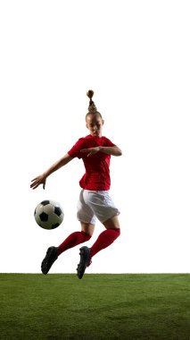 Atletik kız, yeşil sahada beyaz arkaplanla oynanan futbol maçında havada hareketli ve kontrollü bir şekilde tekme atıyor. Spor, hareket, enerji, performans, eğitim becerileri kavramı