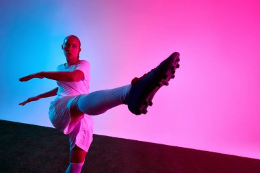 Beyaz futbol formalı bir kadın stüdyo ışıklarının altında güçlü bir şekilde ileri tekme atıyor. Spor, güç, yoğunluk, kontrol, ifade kavramı.