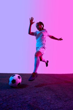 Diz üstü diziyle koşan bayan atlet sahada futbol topunu geçti. Mor renkli arka planda. Spor, hız eğitimi, futbol hareketi, koşu gücü ve kararlılık kavramı.