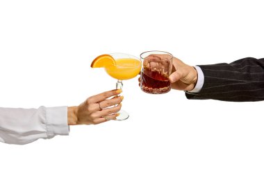 İçkiler aracılığıyla bağlantı. Kadın ve erkek elleri portakal bardakta kokteyl, portakal suyu, turunçgil dilimi ve koyu bir likör karışımı karıştırıyor. Kadeh kaldırma, parti, zarafet, kontrastlık.