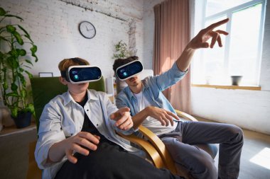 VR kulaklık takan genç bir aile, rahat bir oturma odasında sanal gerçeklik deneyimine tamamen dalmış durumda. Evdeki modern eğlence anlayışı.