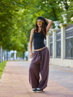 Orijinal titreşimler. Genç sokak dansçısı, ağaçlarla kaplı bir kaldırımda güven içinde poz veriyor. Şehir gençlik kültürü ve kendini ifade etme kavramı dans yoluyla.