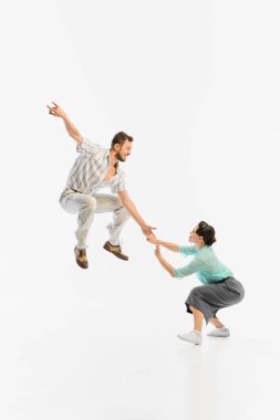 Swing dansçıları, beyaz arka planda klasik kıyafetler içinde havada yakalanır. Retro dans coşkusu ve neşeli hareket kavramı.