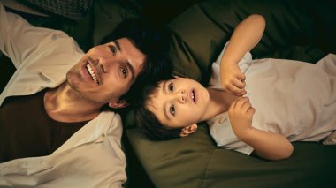 Bir baba ve oğul yatakta kaynaşır, sıcak bir yuva ortamında birlikte güzel vakit geçirirler. Aile bağı kavramı, samimi anlar ve gerçeklik