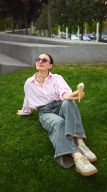 Sakin ol tatlım. Rahat yaşlı kadın, güneşli bir park ortamında çimlerin üzerinde otururken dondurmanın tadını çıkarıyor. Boş zaman, hoşgörü, refah ve düşünceli yaşam kavramı