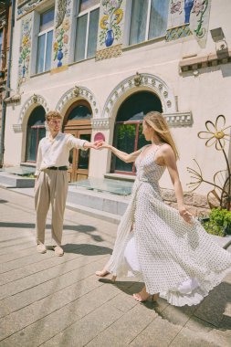 Şehir keşfi. Arkaplan olarak sanatsal bir bina olan bir şehir sokağında neşeyle dans eden bir çift. Şehir romantizmi ve anlamlı hareket kavramı.