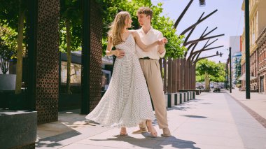 Genç romantik çift güneşli şehir caddesinde zarif yaz kıyafetleriyle neşeyle dans ediyor. Aşk, yaşam tarzı, romantizm, moda, seyahat, mutluluk ve şehir ilişkileri kavramı.