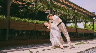 Zahmetsiz bir tarz. Çiftler güneşli bir günde yeşillikli modern bir kafe dışında neşeyle dans ederler. Şehir doğasında tasasız anlar, dans, gençlik kültürü ve moda kavramı