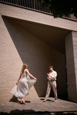 Yavaş yaşam ve dikkatli yaşam tarzı. Güneşli, modern bir şehir mimarisi köşesinde zarif bir şekilde dans eden çift, şehir ortamlarındaki zarafet kavramını vurguluyor..