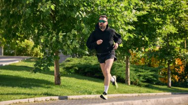 Güneşli bir günde yeşil yaprakların arasında koşan güneş gözlüklü biri. Fiziksel dayanıklılık, tek motivasyon, spor anlayışı, kamusal alan eğitimi ve rekabetçi ruh kavramı..