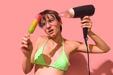 Eriyen gökkuşağı dondurması, saç kurutma makinesi ve yeşil bikini ve gözlük takan kafası karışmış bir kadın. Saçma yaz davranışı, gerçeküstü yemek mizahı, yaratıcı gençlik yaşam tarzı..