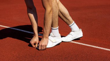 Atlet, parlak güneş ışığı altında kırmızı pist yüzeyinde koşmaya hazırlanıyor. Hareket başlatma kavramı, yüzey dokusunu izleme, eğitim başlangıcı, hazırlık anı