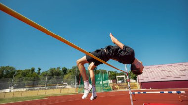Sporcu açık mavi gökyüzünün altında yüksek atlama yapıyor. Kutup kavrama tekniği, atlama mekaniği, giriş hazırlığı, spor performansı kavramı