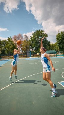 Açık bir gökyüzünün altındaki açık bir sahada bir çift kadın, rekabetçi basketbol oynuyor. Spor, yükselen hareket markalaşması, basketbol yaşam tarzı kampanyalarında yüksek kadın kararlılığı hedefleme kavramı