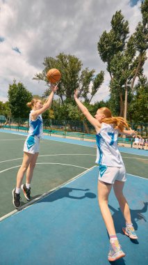 Açık hava sahasında güneş ışığıyla yıkanan iki kadın heyecanlı bir basketbol maçına katılıyor. Beceri ve tepki kavramı, basketboldaki gençlik rekabeti, yüksek enerji fitness, spor eğitimi promosyonu