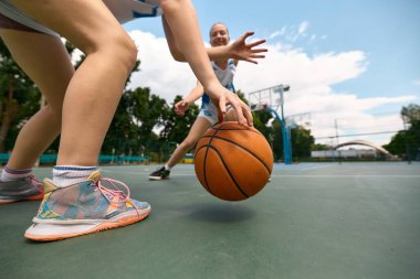 Kadınlar açık hava sahasında gündüz yapılan bir basketbol maçına katılıyorlar. Aksiyon anlayışı, kadın basketbol gücü, spor markalaşması, hızlı gençlik görselleri.