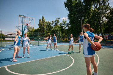 Aydınlık bir günde bayan basketbol takımı dışarıda yarışıyor. Isınma pozisyonu kavramı, basketbol talimine hazırlanan kızlar, spora hazır olmak, gençlik hayatında spor yapmak, açık hava aktiviteleri.
