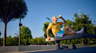 Spor giyim sektöründe yaşlı bir adam spor salonundaki antrenmandan sonra su içiyor. Eğitim sonrası su kaybı, sağlıklı alışkanlıklar, yaz sporları, enerji iyileştirme, sağlık yaşam tarzı..