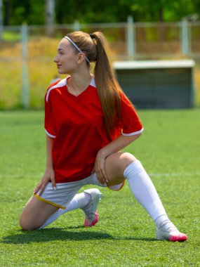 Genç bayan futbolcu güneş ışığında çimenlik alanda geriniyor. Bencil odaklanma ve spor farkındalığı, konsantrasyon ve beden hizalaması kavramı.