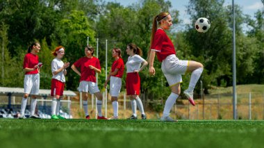 Kadın futbol takımı mavi gökyüzünün altındaki çimlerde antrenman yapıyor. Kadın sporlarında eğitim günü kavramı, gençlerin spor markalaşması ve işe alınması için gerçek yaşam pratiği anları.