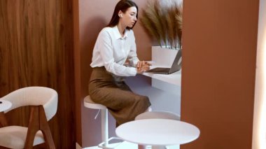 Kablosuz kulaklıklı bir kadın modern yüksek masada otururken bilgisayarda danışmanlık yapıyor. Çevrimiçi konferans konsepti, iş koçluğu, serbest çalışma, kadın liderliği.