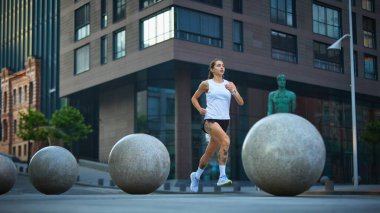 Modern binaların yakınında küresel heykellerle şehir merkezinde koşan bir kadın. Kentsel fitness 'te güç ve kadınlık kavramı, tasarım ve fiziksel hareketlerde denge.