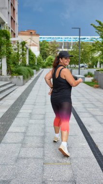 Şehir kaldırımında yürürken gülümseyen bir kadın. Özgüven, sağlıklı yaşam tarzı, vücut pozitifliği ve şehir özgürlüğü kavramı..