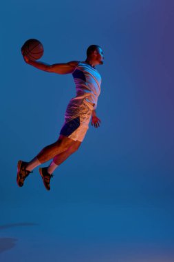 Basketbol atleti canlı neon ışıklar altında güçlü bir smaç basıyor. Uçuş ve gölge kavramı, anlamlı performans, basketbol sanatı ve yüksek kontrastlı kimlik medyası.