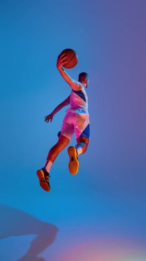 Basketbolcu canlı mavi zemine karşı havada sıçrıyor. Çevik hareket kavramı, neon ışıklı uçuş, atletik performans ve gençlik hedefli spor markalaşması..
