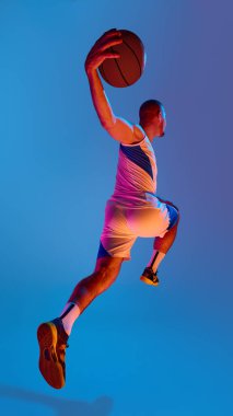 Dinamik basketbolcu mavi arka planda smaç basmak için sıçrıyor. Yukarı doğru hareket kavramı, iç güç, sporda erkeksi enerji, ve sinematik spor editör hareketi.