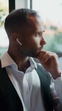 Modern kafede, odaklanmış yüzü ve kablosuz kulaklığı olan bir laptop kullanan girişimci. Serbest çalışma kavramı, kişisel marka geliştirme, iş koçluğu, SMM ve fintech.