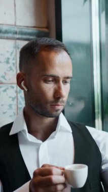 Kafe penceresinde bir fincan kahve ve açık hava manzaralı bir bilgisayarda çalışan bir adam. Ortak çalışma ortamı kavramı, gevşetilmiş üretkenlik, çevrimiçi odaklanma, serbest çalışma ve uzak iş kültürü kavramı.