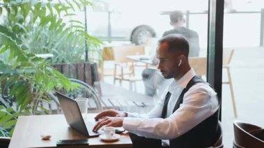 Beyaz gömlekli ve yelekli bir iş adamı ciddi bir ifadeyle laptop ekranına bakıyor. İş yönetimi kavramı, çevrimiçi işbirliği, sanal toplantılar ve teknoloji güdümlü serbest çalışma rutini.