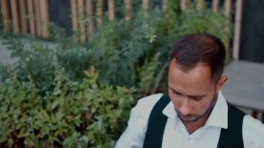 Kulaklıklı bir adam yazlık terasta kafede tablet üzerinde çalışıyor. Uzaktan işbirliği, serbest verimlilik, mobil işyeri ve dijital iş akışındaki konsantrasyon kavramı.