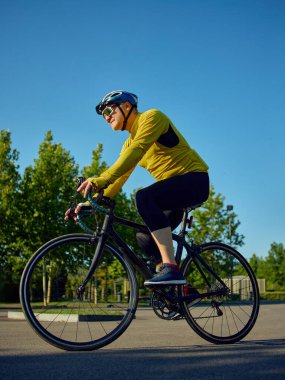 Açık güneşli bir sabahta şehir parkında bisiklete binen odaklanmış son sınıf bisikletçi. Sağlıklı rutin, spor yapma alışkanlığı, dayanıklılık geliştirme, olgun yetişkinler için açık hava yaşam tarzı kavramı.