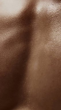 Pürüzsüz erkek gövdesine yakın çekim. Görünür deri dokusu ve sıcak gölgeleri var. Vücut terapisi görselleri, erkek cilt markası, sağlık dergisi düzeni ve somatik farkındalık araçları kavramı.